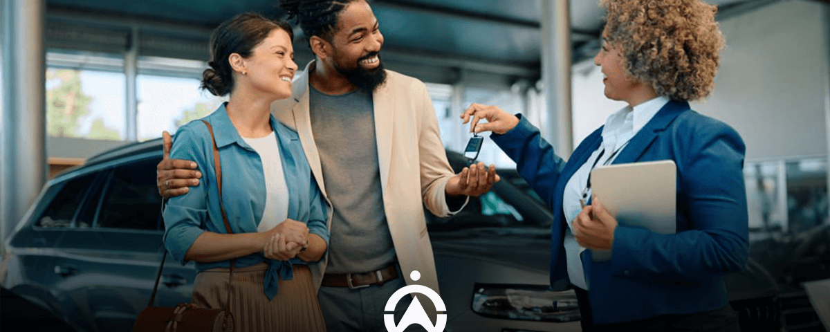 A couple happily interacts with a saleswoman at a car dealership, discussing keys in front of a parked vehicle.
