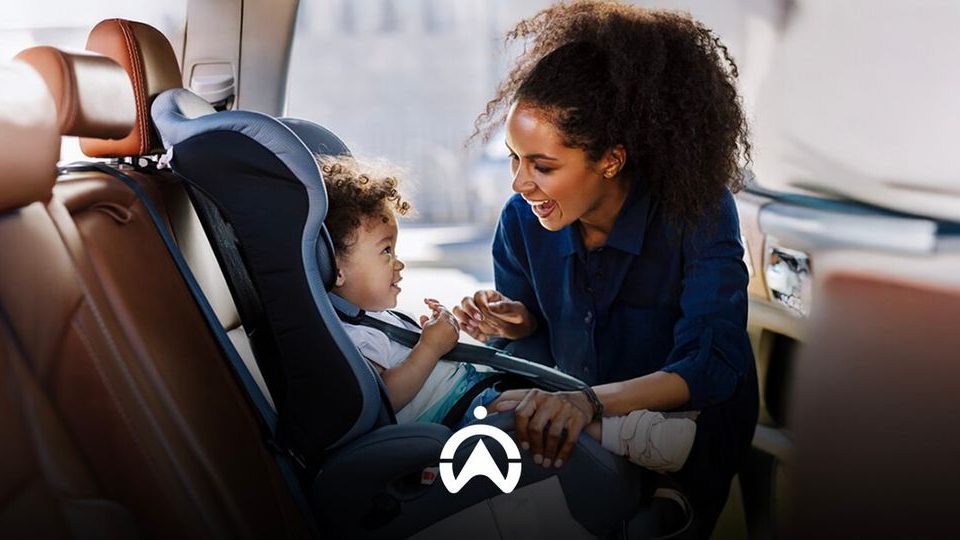 A caregiver interacts with a child in a car seat, showcasing a caring moment in a vehicle's back seat.
