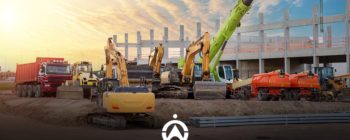 A construction site at sunset featuring various heavy machinery, including excavators and trucks, near a concrete structure.