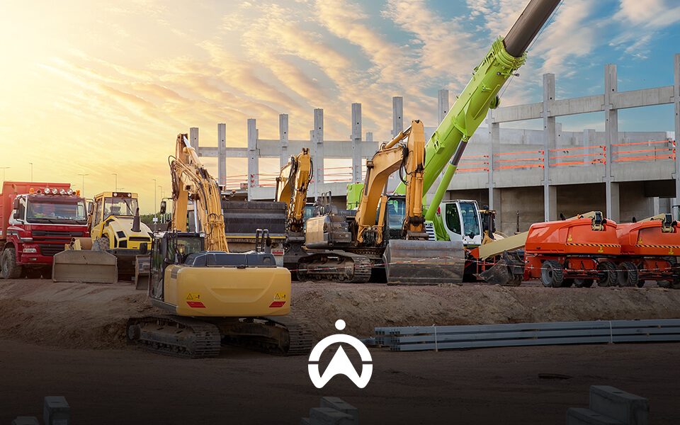 A construction site at sunset featuring various heavy machinery, including excavators and trucks, near a concrete structure.