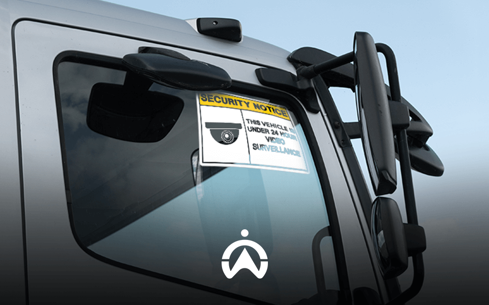 A close-up of a truck’s side mirror displaying a security notice about 24-hour video surveillance.