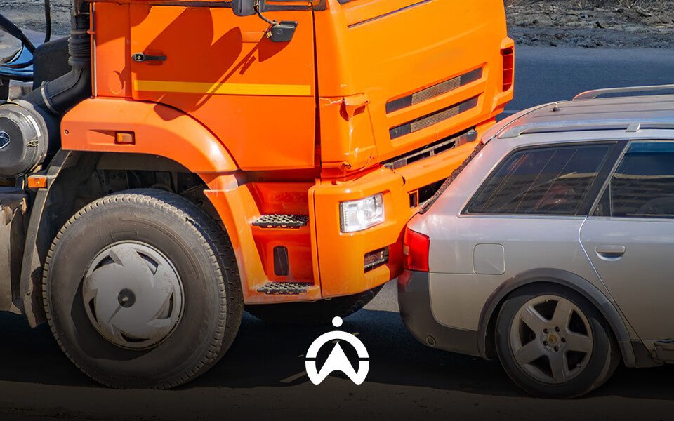 A front view of a collision between an orange truck and a silver car, highlighting damage to both vehicles on a road.
