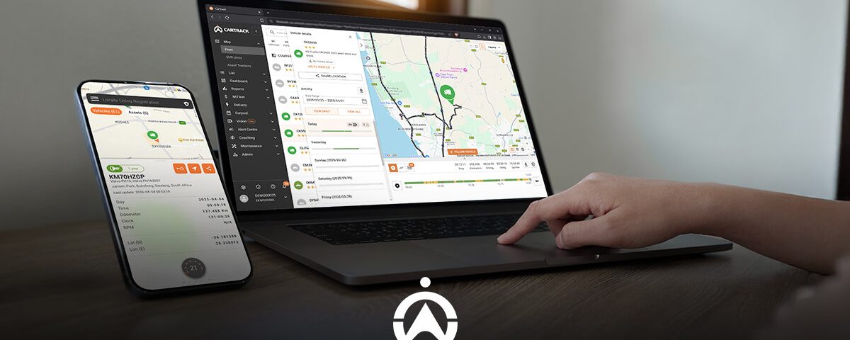 A person uses a laptop and smartphone displaying a vehicle tracking application, with a map and vehicle details visible on the screen.