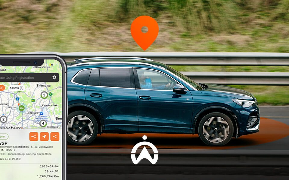 A blue Volkswagen SUV drives past a highway railing, with a smartphone displaying a vehicle tracking map and location pin.