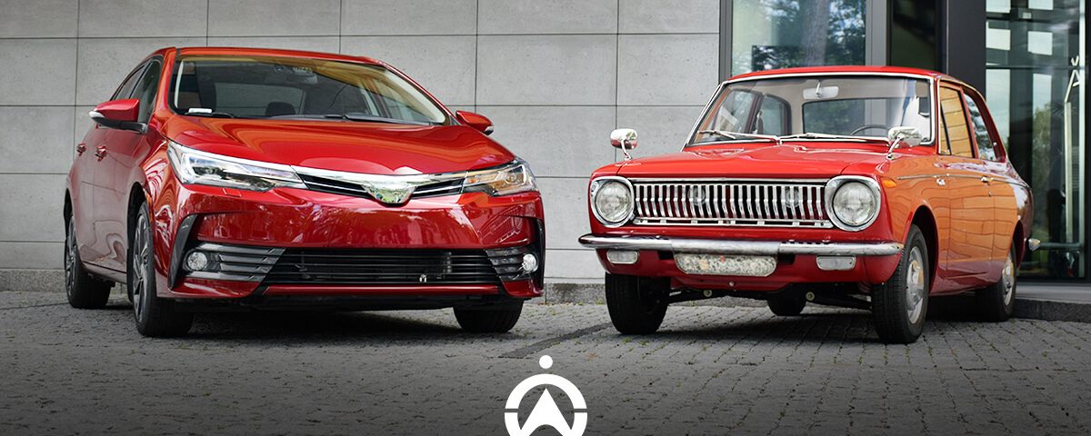 A modern red sedan and a classic red car are parked side by side, showcasing the evolution of automotive design.
