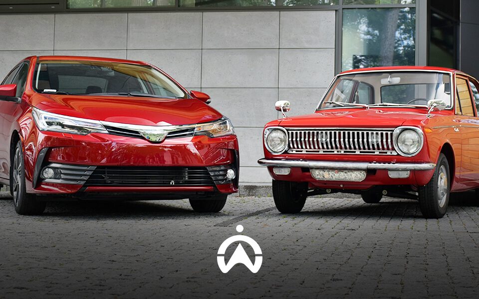 A modern red sedan and a classic red car are parked side by side, showcasing the evolution of automotive design.