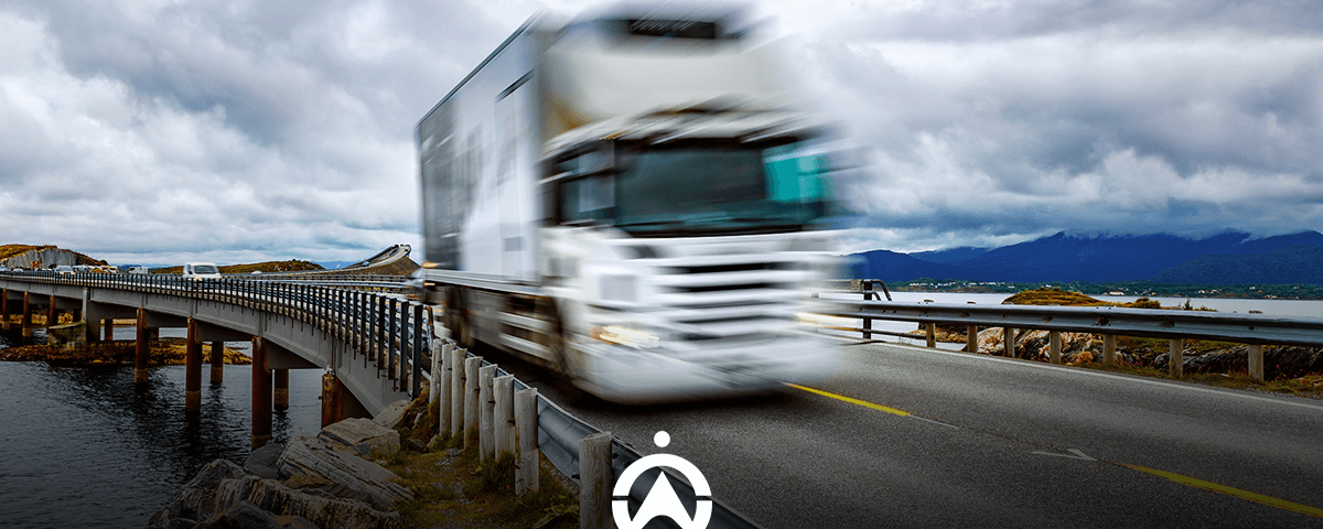 A blurred white truck speeds over a curved bridge by a body of water under a dramatic sky, symbolizing motion and transport.