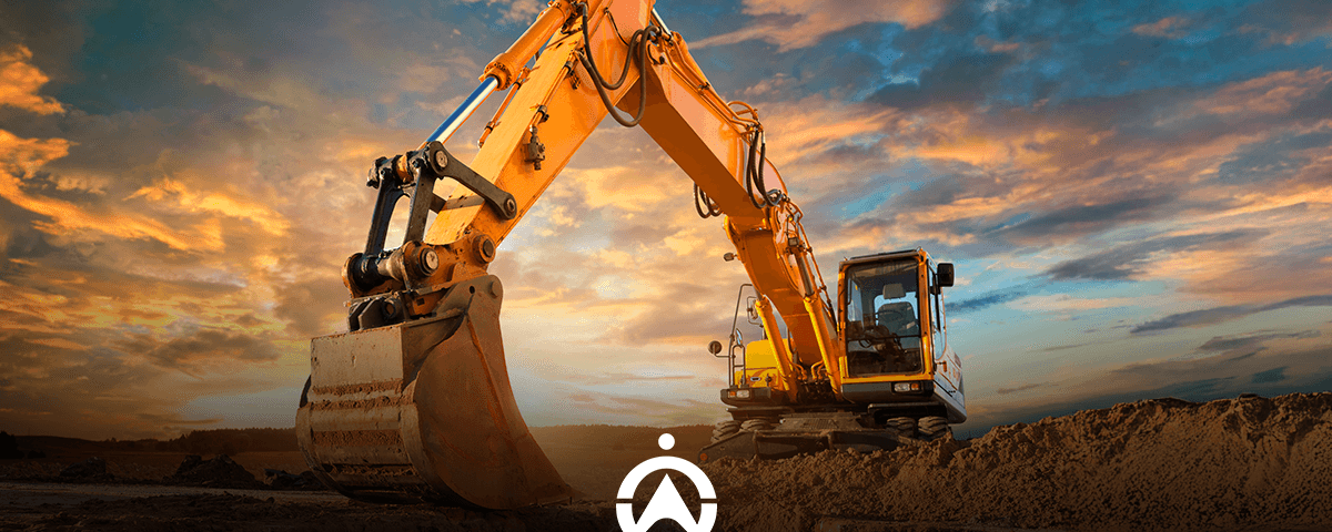 A bright yellow excavator with a large bucket, set against a dramatic sunset sky, prepares to dig into a sandy ground.