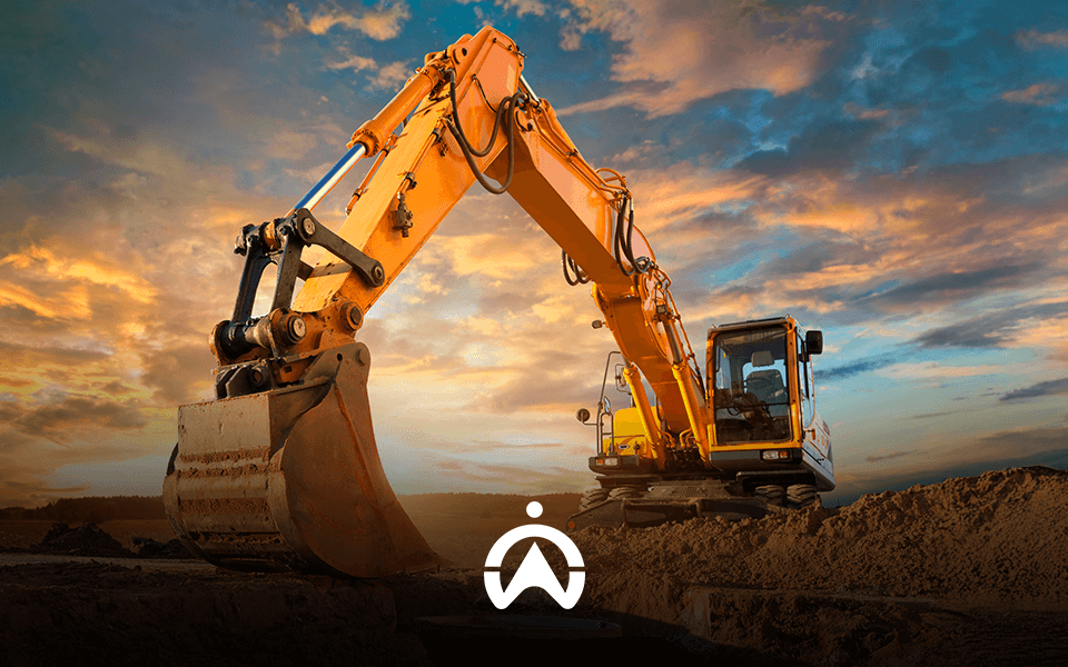 A bright yellow excavator with a large bucket, set against a dramatic sunset sky, prepares to dig into a sandy ground.