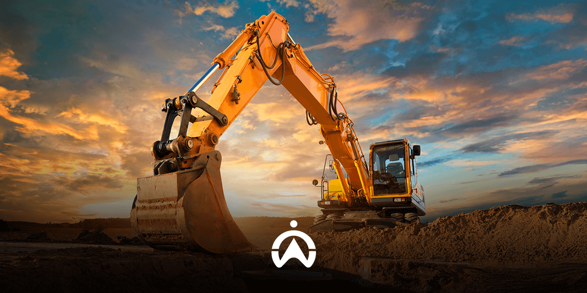 A bright yellow excavator with a large bucket, set against a dramatic sunset sky, prepares to dig into a sandy ground.