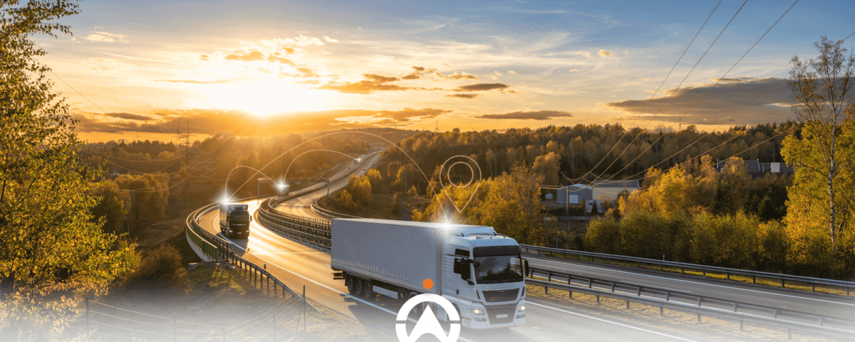 Two trucks drive along a winding road at sunset, surrounded by trees and power lines, symbolizing transport and connectivity.