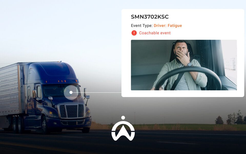 A blue semi-truck drives along a highway, while a digital alert indicates "Driver: Fatigue" next to a video of the driver.