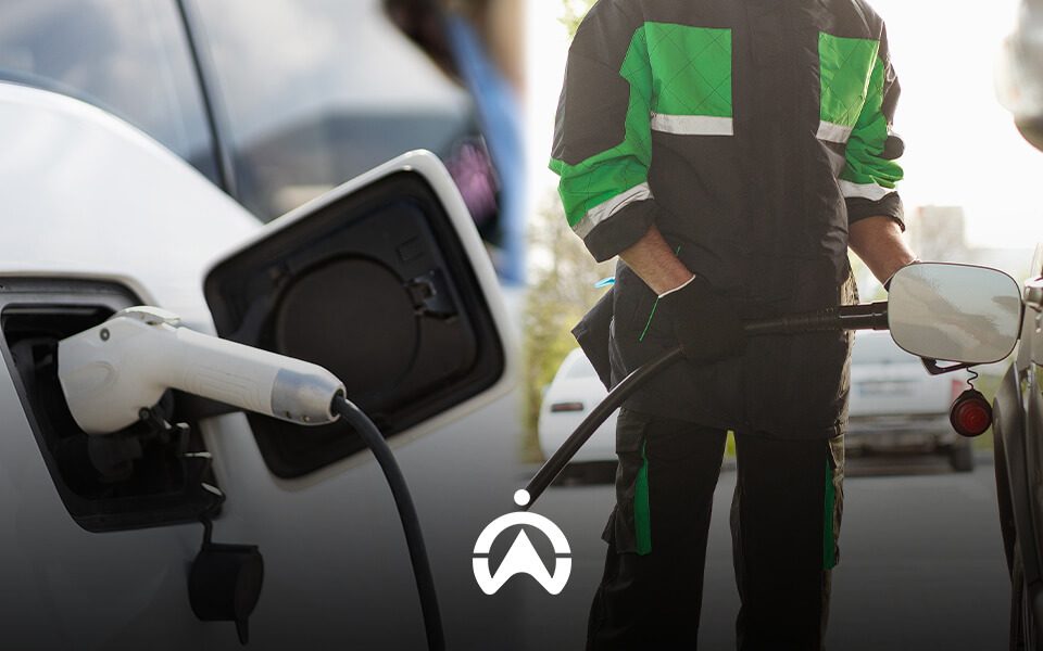 A technician wearing a black and green uniform refuels a vehicle while an electric charging cable is connected to another car.